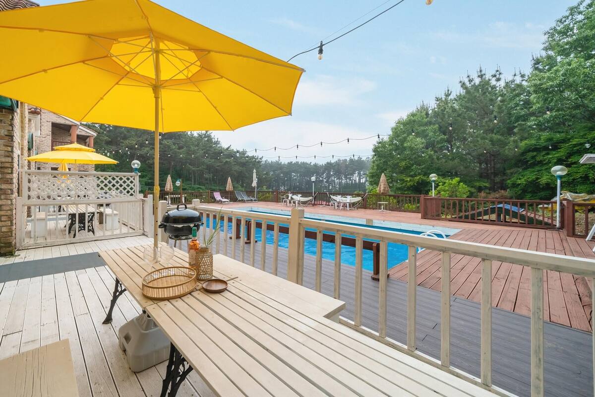 A wooden deck with a pool, outdoor furniture, and a yellow umbrella.