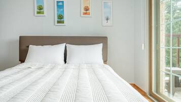 Una cama con colcha blanca y almohadas, cabecera marrón y cuadros en la pared.