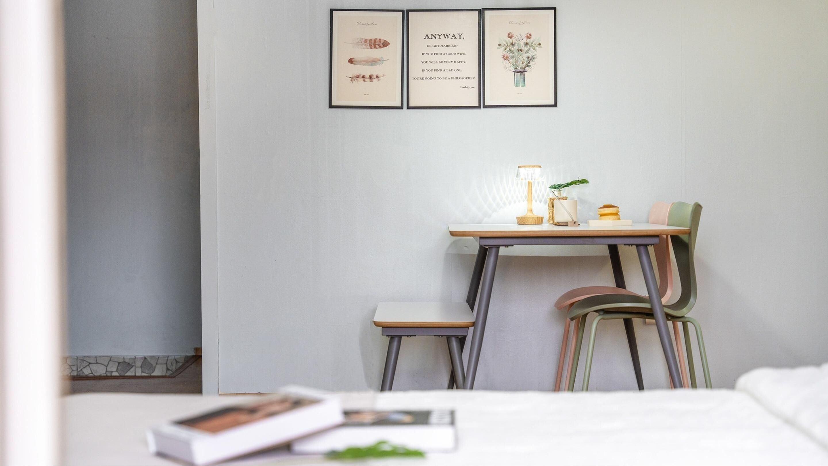 A neatly arranged hotel room with a bed, a small desk with a lamp, a chair, and a framed quote on the wall.