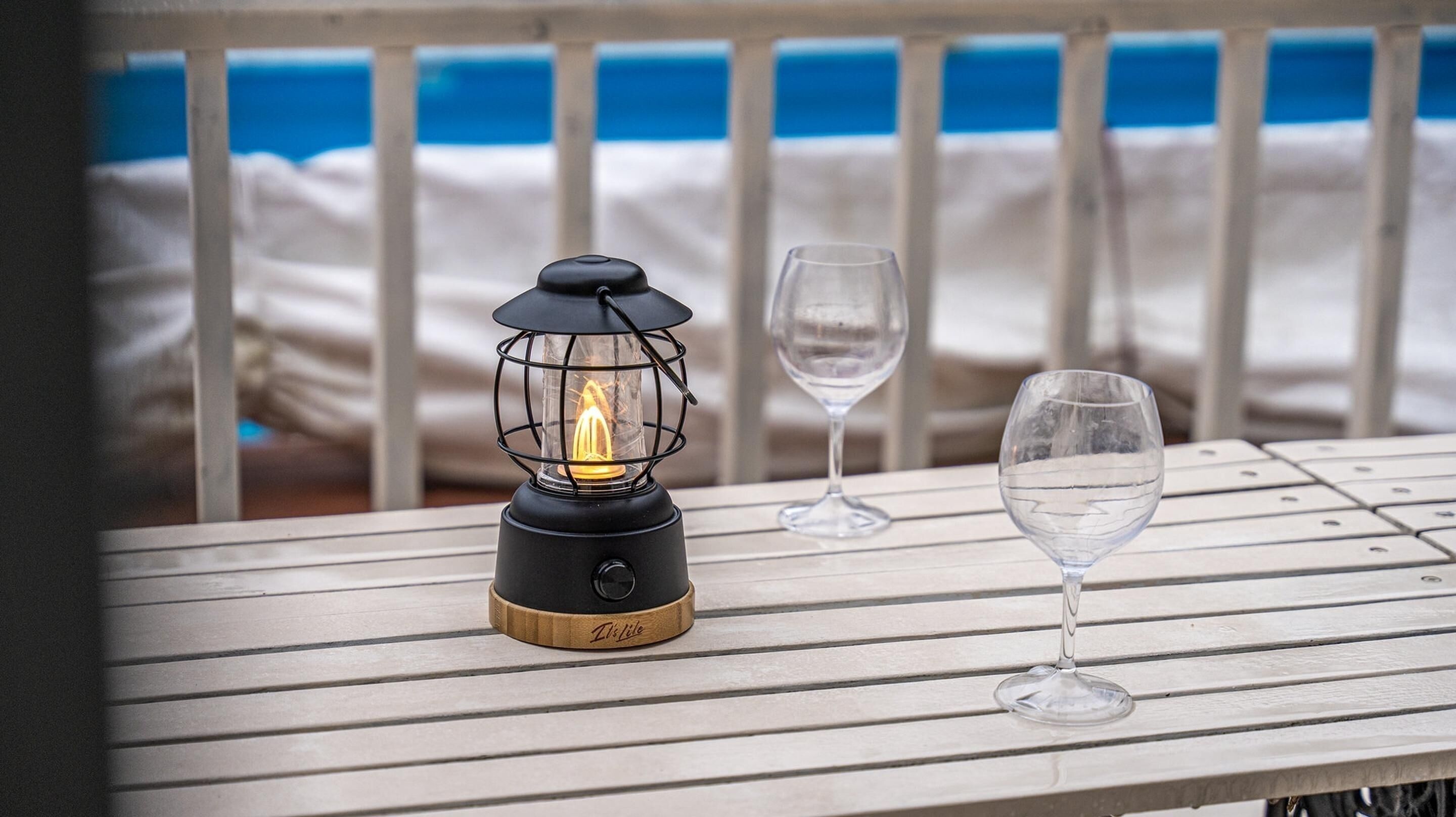 Mesa com lanterna e dois copos, montada junto a um corrimão com vista para o mar.
