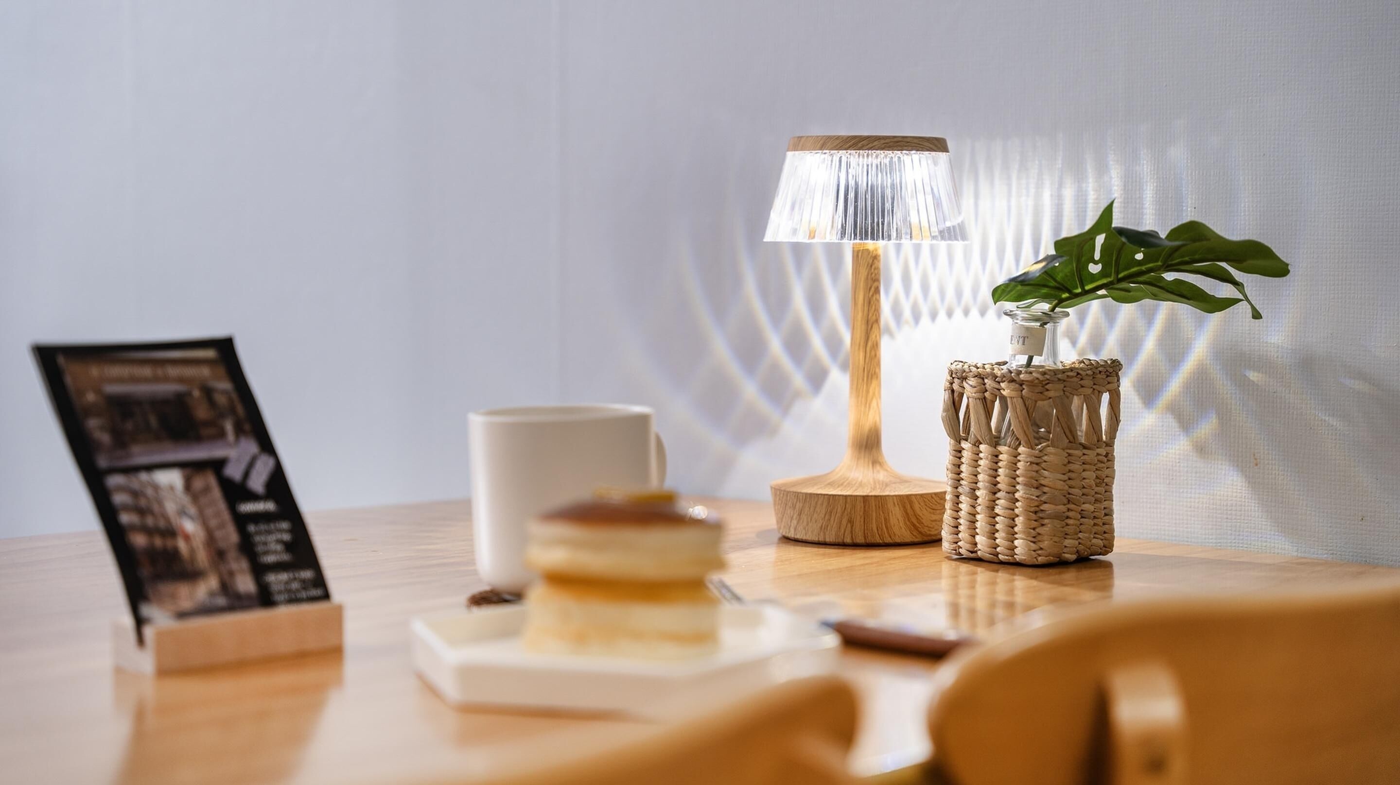 A wooden table with a lamp, a white mug, a small plant in a woven basket, and a framed picture.
