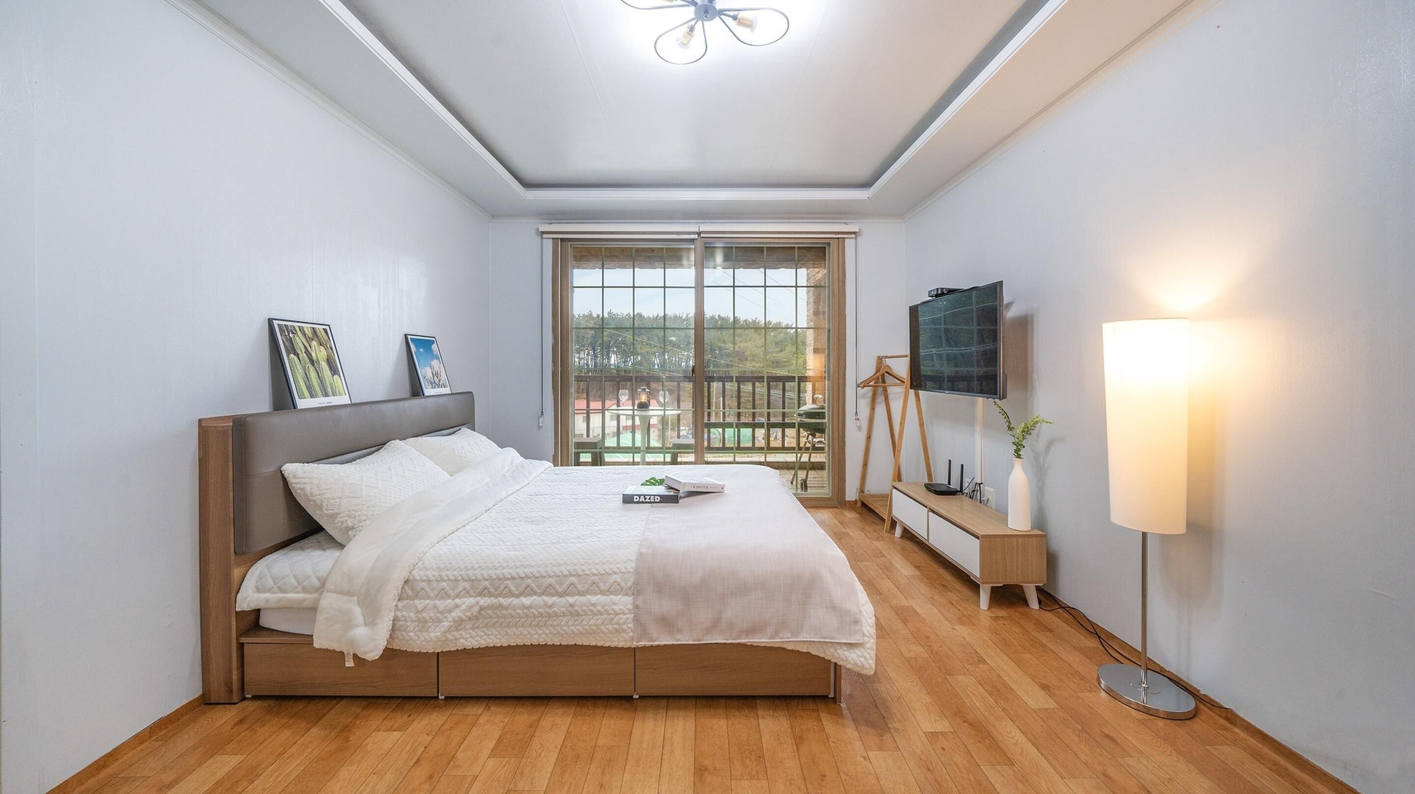 Un dormitorio moderno con una cama, un televisor, una mesita de noche y una ventana con vistas.