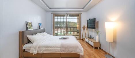 Un dormitorio moderno con una cama, un televisor, una mesita de noche y una ventana con vistas.