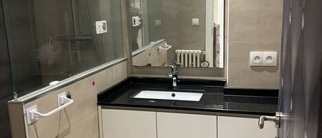 A modern bathroom with a glass shower enclosure, a sink with a mirror above it, and a white tiled floor.