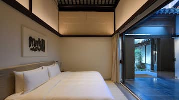 A modern bedroom with a large bed, a headboard, a wall-mounted artwork, and a sliding glass door leading to an outdoor area.