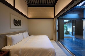 Een moderne slaapkamer met een groot bed, een hoofdbord, een aan de muur bevestigd kunstwerk en een schuifdeur naar buiten.