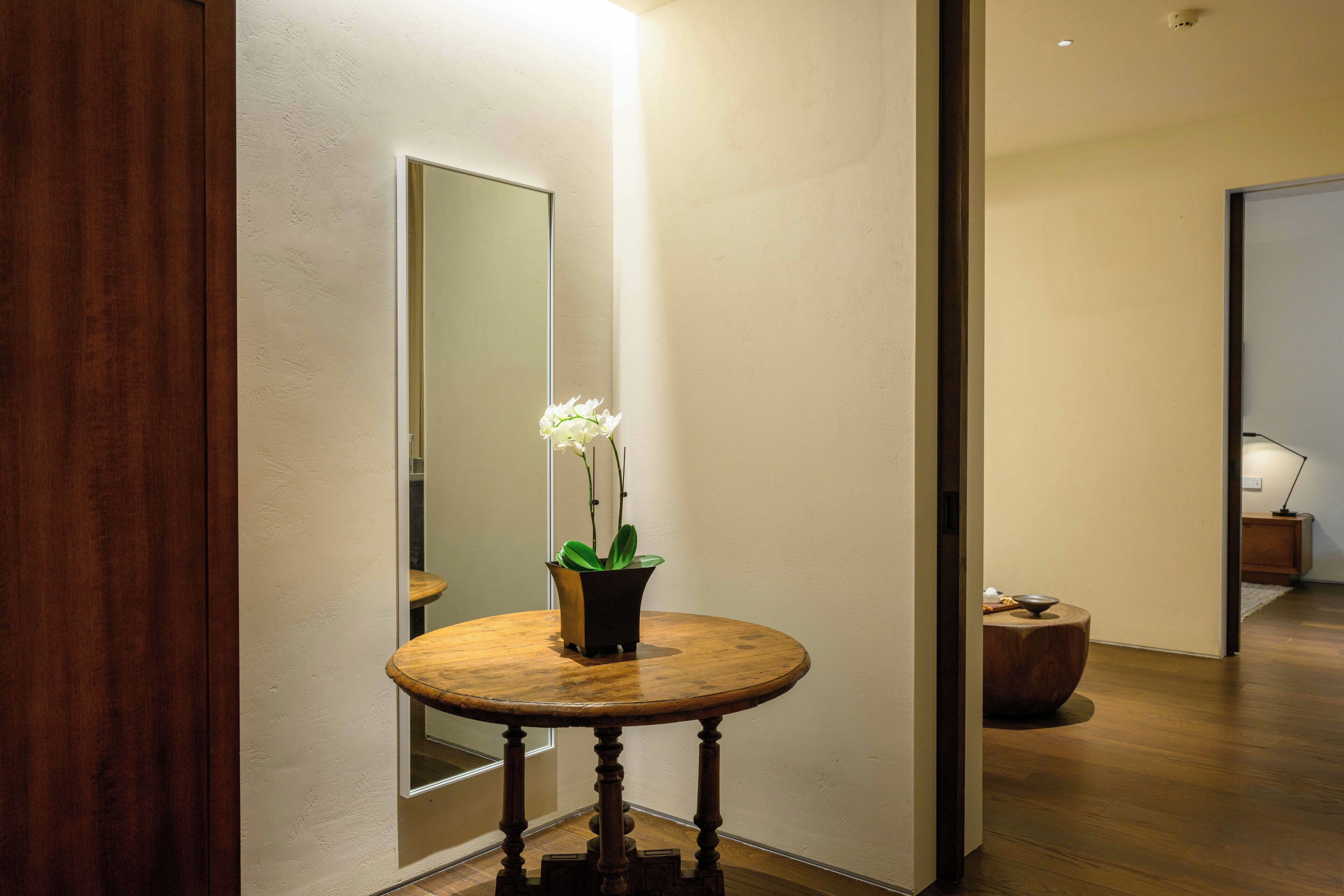 A hallway with a round wooden table, a potted orchid, and a mirror on the wall.