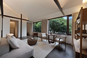 Een moderne woonkamer met een bank, stoelen, een salontafel en een groot raam met uitzicht op bomen.