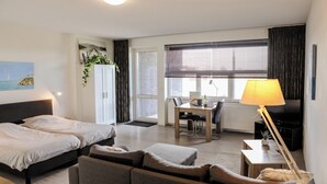 A hotel room with a bed, a sofa, a dining table, a TV, and a window with curtains. - Appartement 16 Wemeldinge (Wemeldinge)