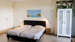 A bedroom with a bed, bedside lamps, a wardrobe, and a painting on the wall. - Appartement 16 Wemeldinge (Wemeldinge)