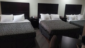 Habitación de hotel con tres camas, cada una con una colcha estampada, una mesita de noche con un teléfono y una lámpara de pared.