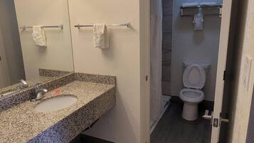 A bathroom with a granite countertop sink, a mirror with lights, a towel rack, and a toilet.