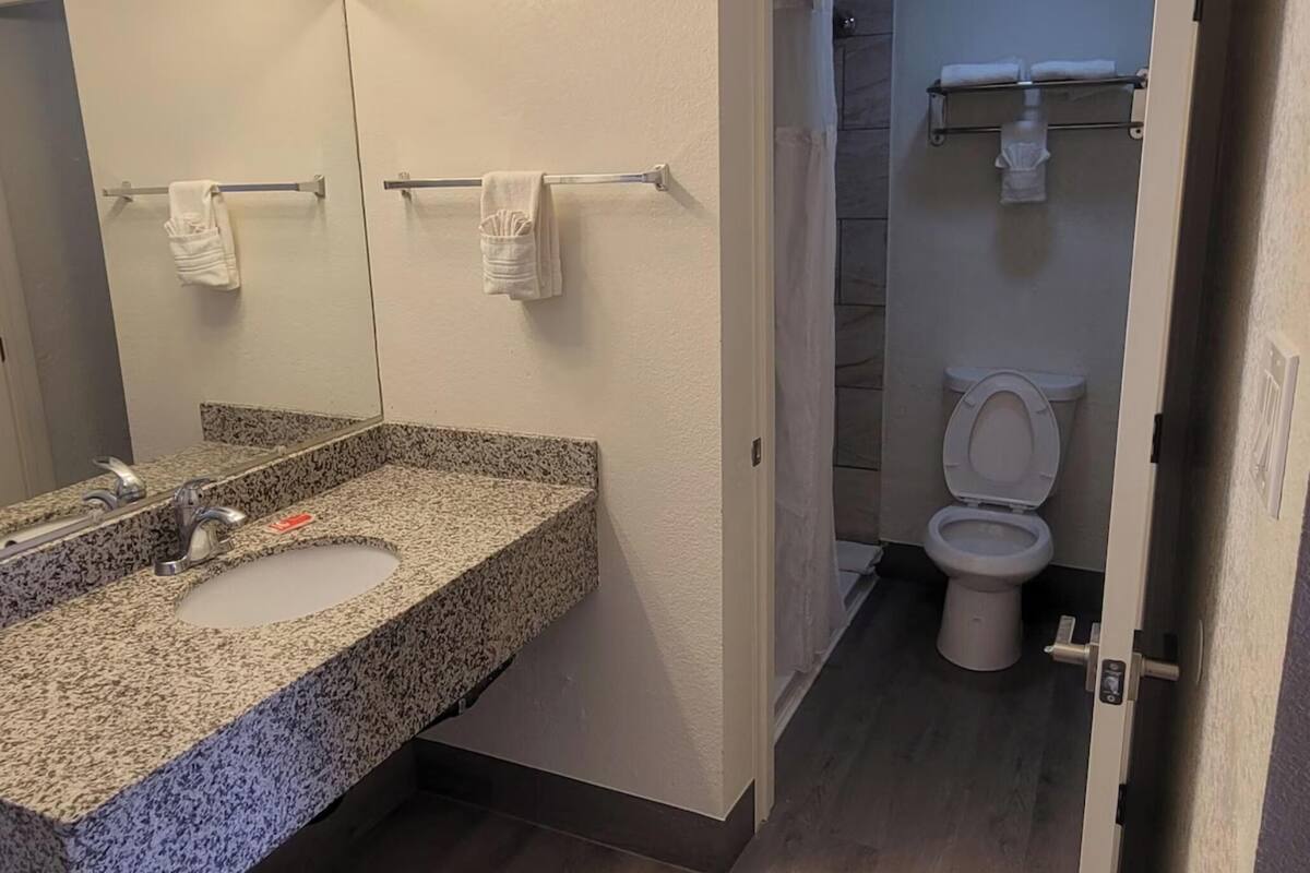 Une salle de bain avec un lavabo doté d’un plan de travail en granit, un miroir avec éclairage intégré, un porte-serviettes et des toilettes.