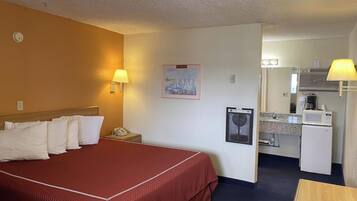 A hotel room with a bed, bedside lamps, a small desk with a microwave, and a painting on the wall.