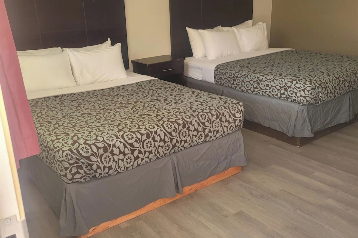 Zwei Betten mit gemusterten Bettwäsche, ein Nachttisch und eine Deckenleuchte in einem Hotelzimmer.
