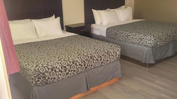 Two beds with patterned bedding, a nightstand, and a ceiling-mounted light fixture in a hotel room.