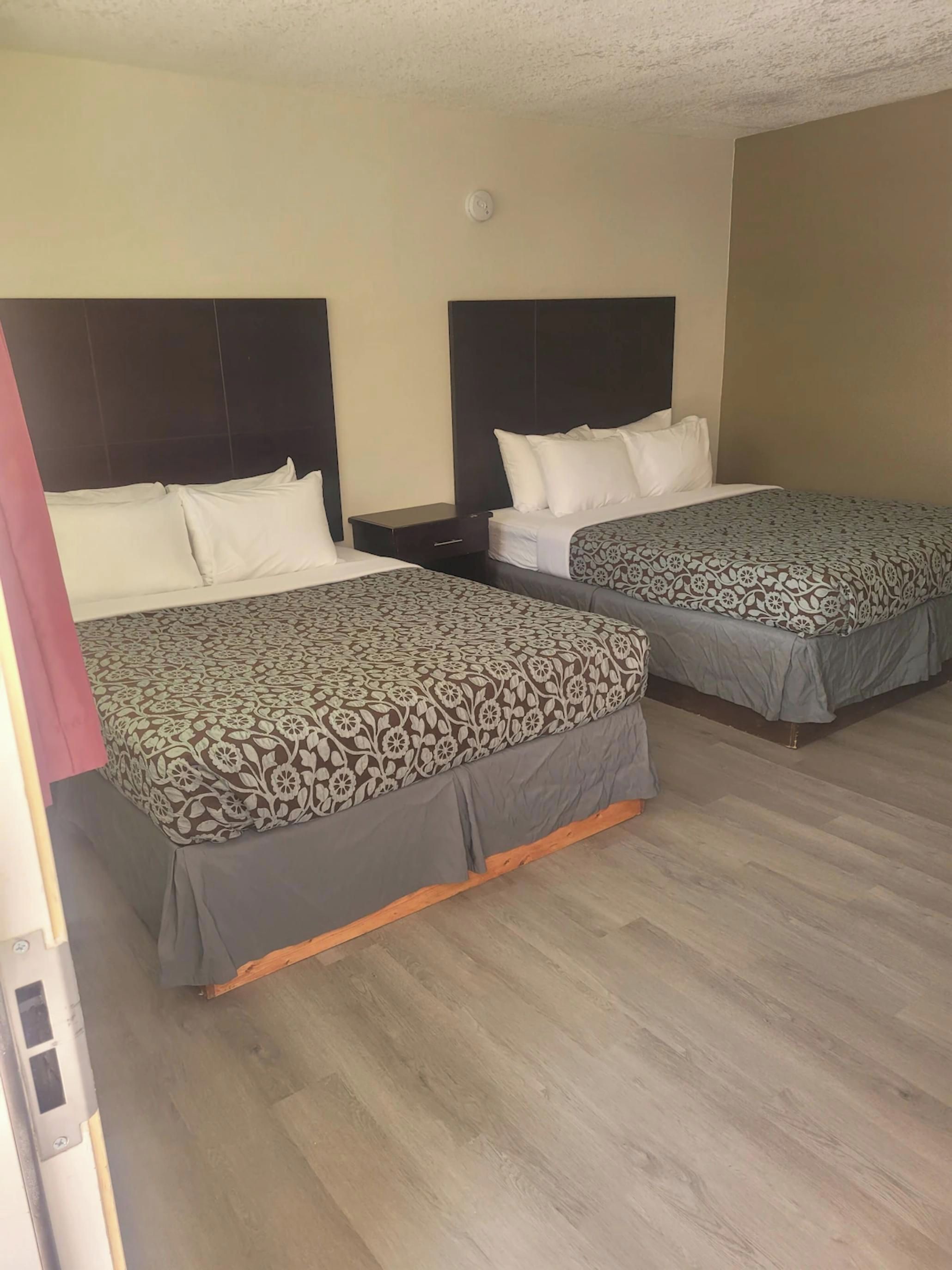 Duas camas com roupa de cama estampada, uma mesa de cabeceira e uma luminária no teto em um quarto de hotel.