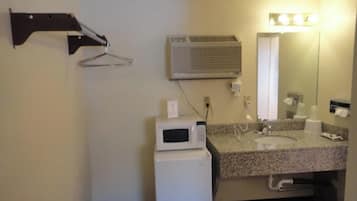 Un baño pequeño con microondas, lavamanos y espejo.