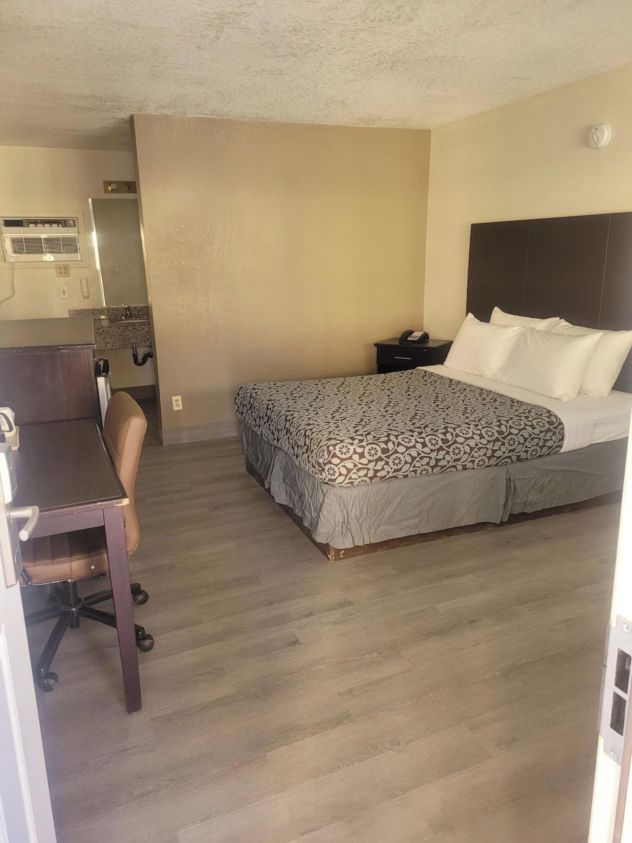 A hotel room with a bed, a desk, a chair, a nightstand, and a bathroom.