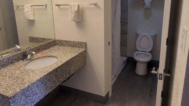 Un baño con lavamanos de encimera de granito, espejo con iluminación, toallero y retrete.