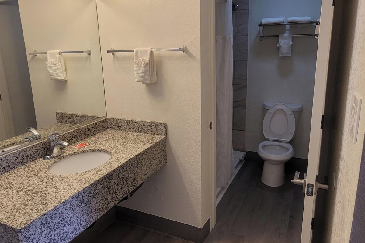 A bathroom with a granite countertop sink, a mirror with lights, a towel rack, and a toilet.