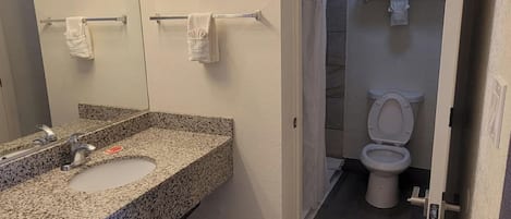 A bathroom with a granite countertop sink, a mirror with lights, a towel rack, and a toilet.