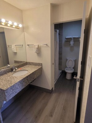A bathroom with a granite countertop sink, a mirror with lights, a towel rack, and a toilet. - Econo Lodge Las Vegas Nm (Las Vegas)