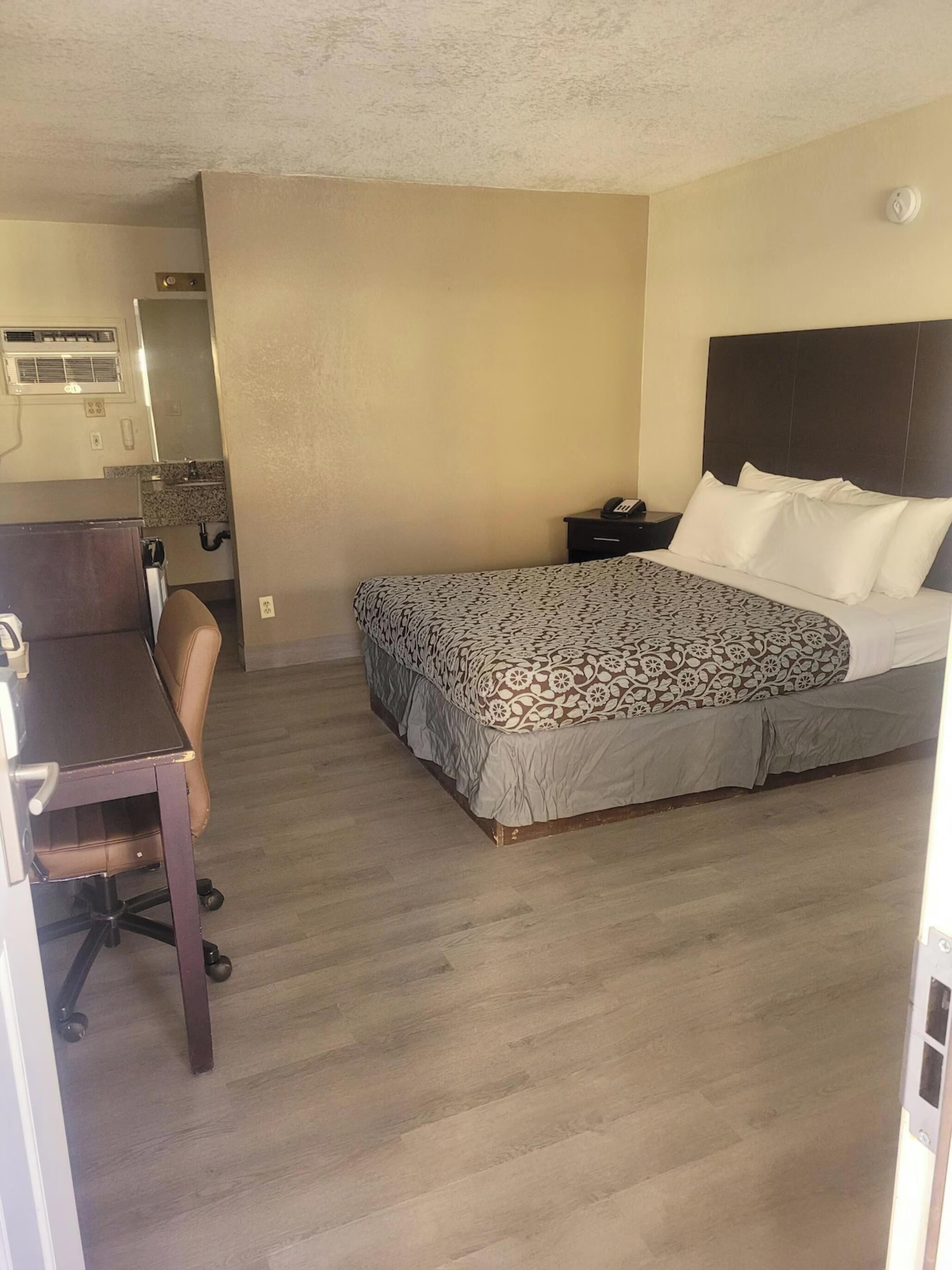 A hotel room with a bed, a desk, a chair, a nightstand, and a bathroom.