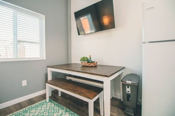 A small kitchen with a wooden table, bench, and a TV mounted on the wall.