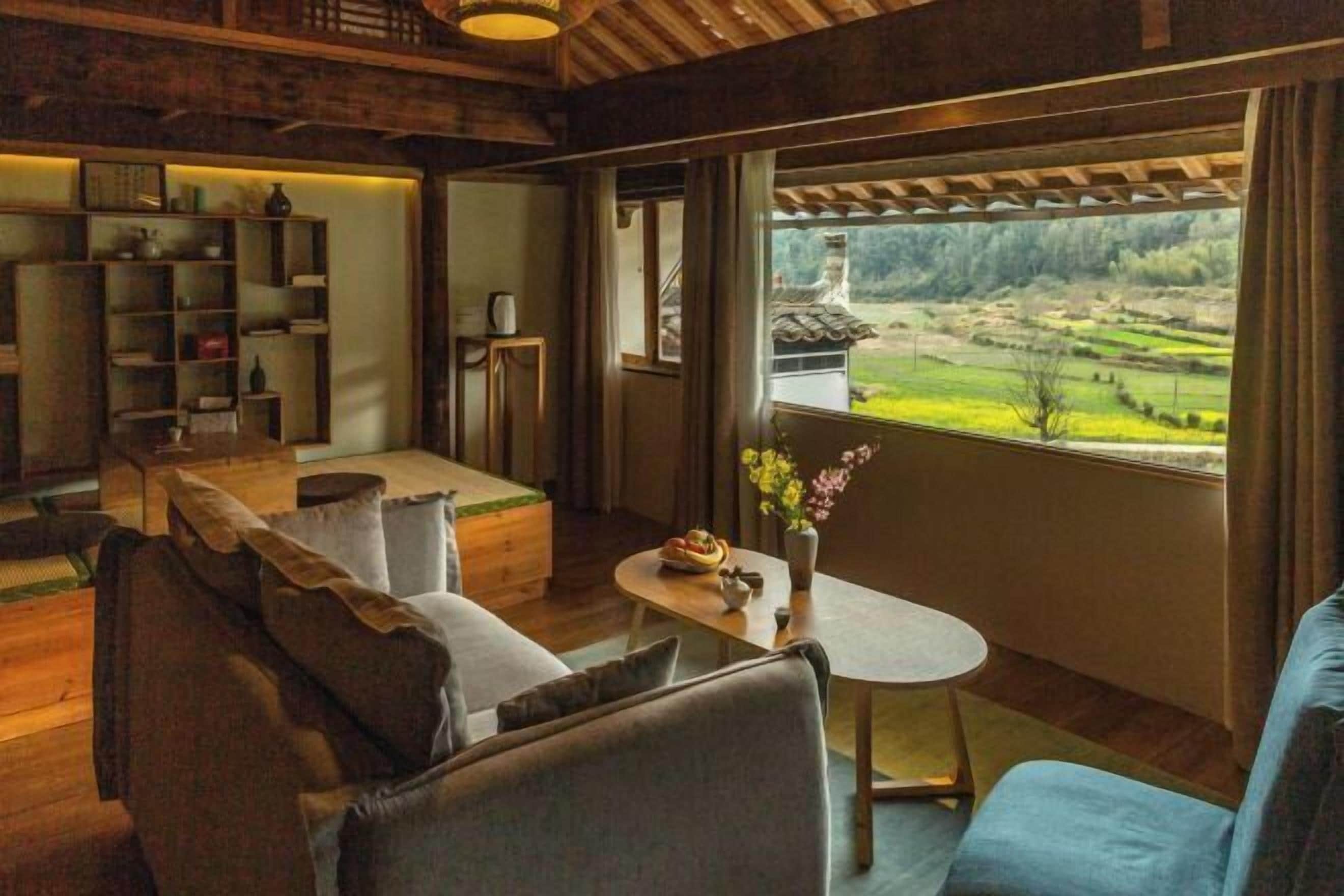 A cozy room with a wooden ceiling, a sofa, a small table, and a view of a green landscape.