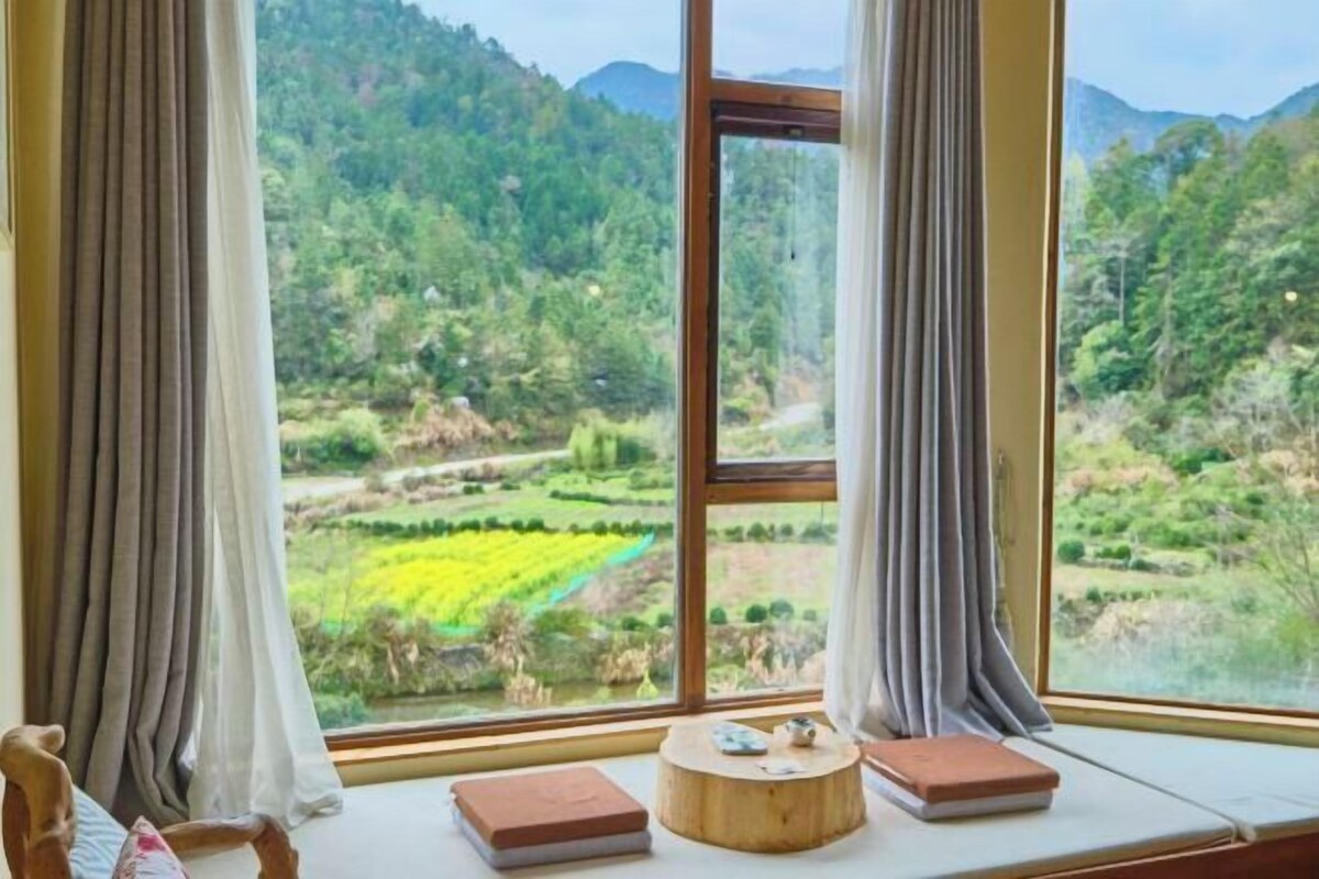 Una habitación con un ventanal que ofrece vistas a un paisaje verde con árboles y colinas.