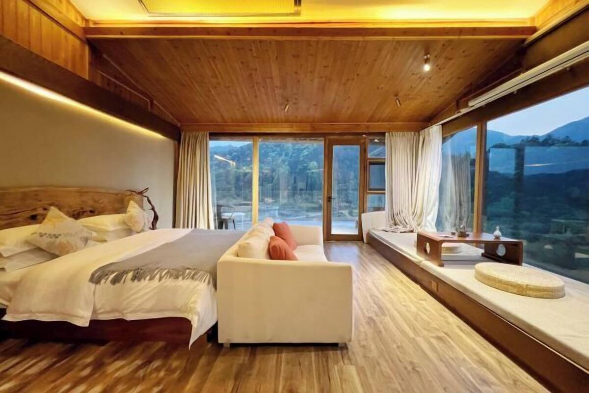 A bedroom with a bed, a sofa, a window seat, and a view of the outdoors.