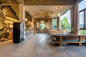 Un intérieur spacieux comprenant un espace salon central, un comptoir de bar et de grandes fenêtres qui laissent entrer la lumière naturelle et offrent une vue dégagée.