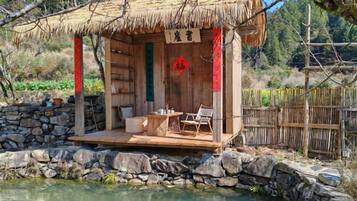 A traditional wooden structure with a thatched roof, a stone wall, and a small pond with koi fish.