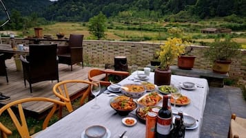 An outdoor dining area with a table set for a meal, surrounded by chairs, with a scenic view of a forested landscape.