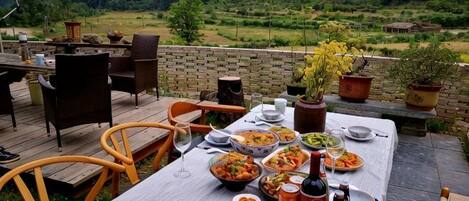 Un área de comedor al aire libre con una mesa lista para una comida, rodeada de sillas y una vista panorámica de un paisaje boscoso.