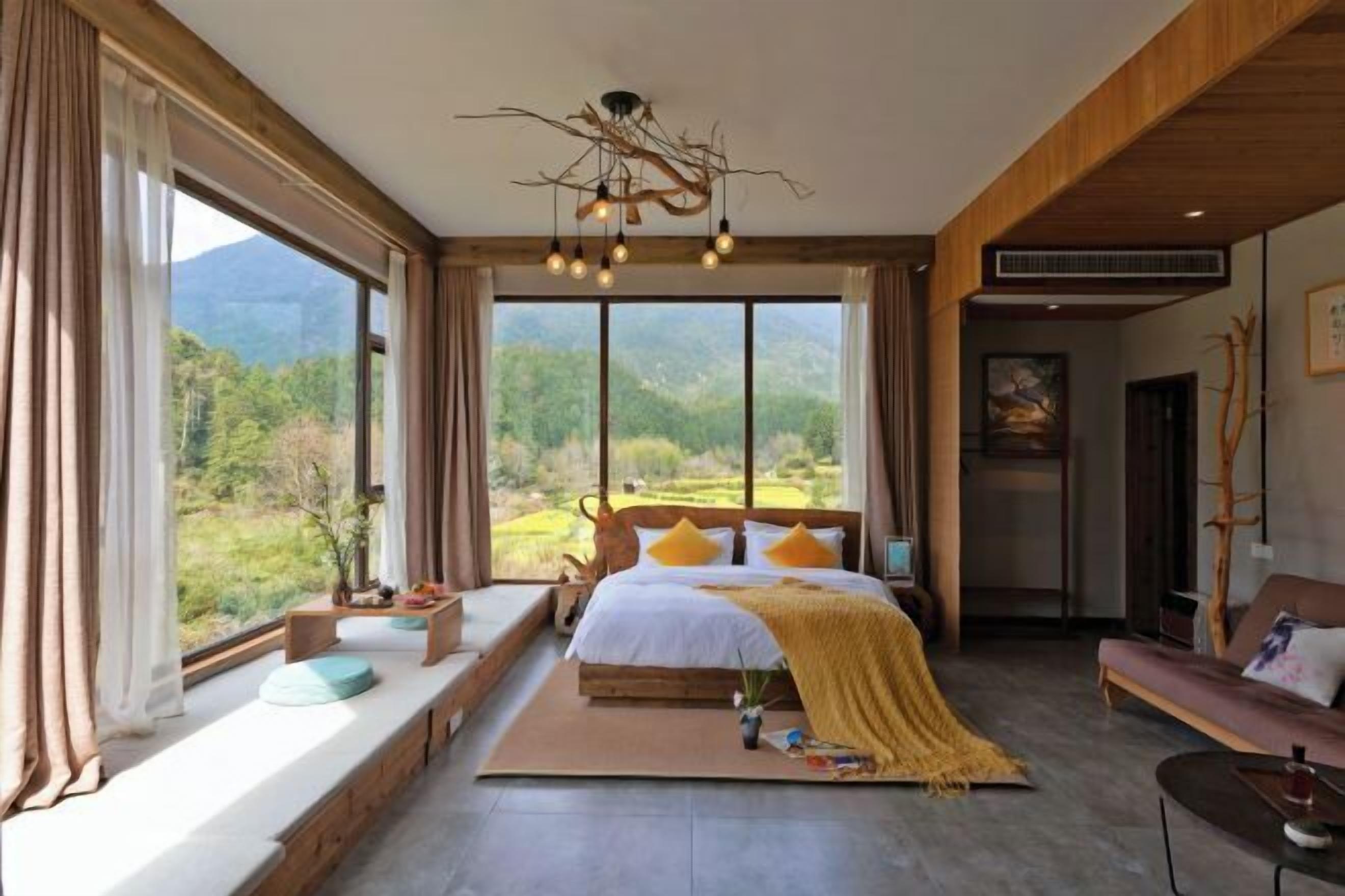 A bedroom with a large window, a bed with pillows, a bedside table, and a sofa.
