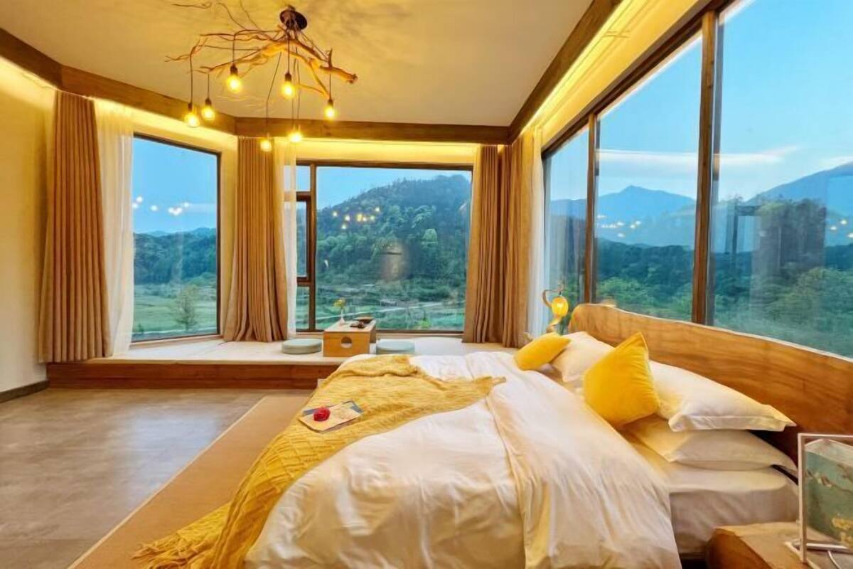 A bedroom with a large bed, a view of the outdoors, and a unique ceiling light fixture.