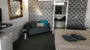 A hotel room with a bed, a sofa, a small table, a mirror, and a bathroom visible through an open door.