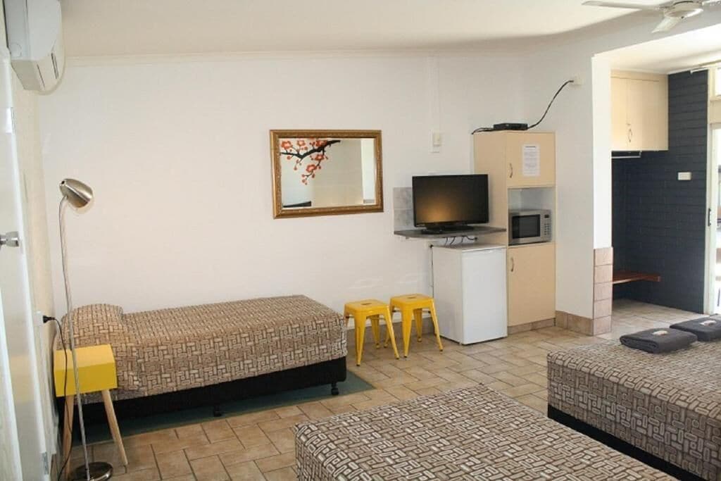 Una habitación compacta con dos camas, un escritorio con televisor, un microondas y una pequeña kitchenette.