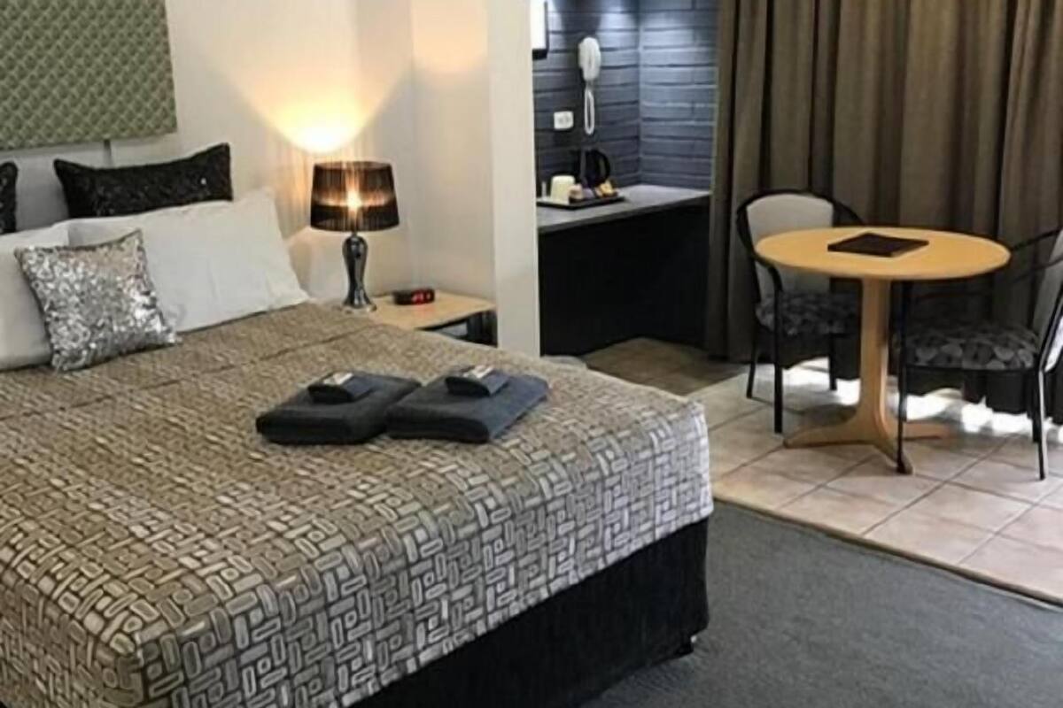 Een hotelkamer met een bed, een bureau met stoel, een plafondventilator en een telefoon.