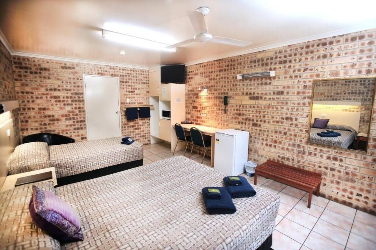 Een kamer met twee bedden, een bureau, een stoel, een kleine koelkast en een spiegel aan de bakstenen muur.