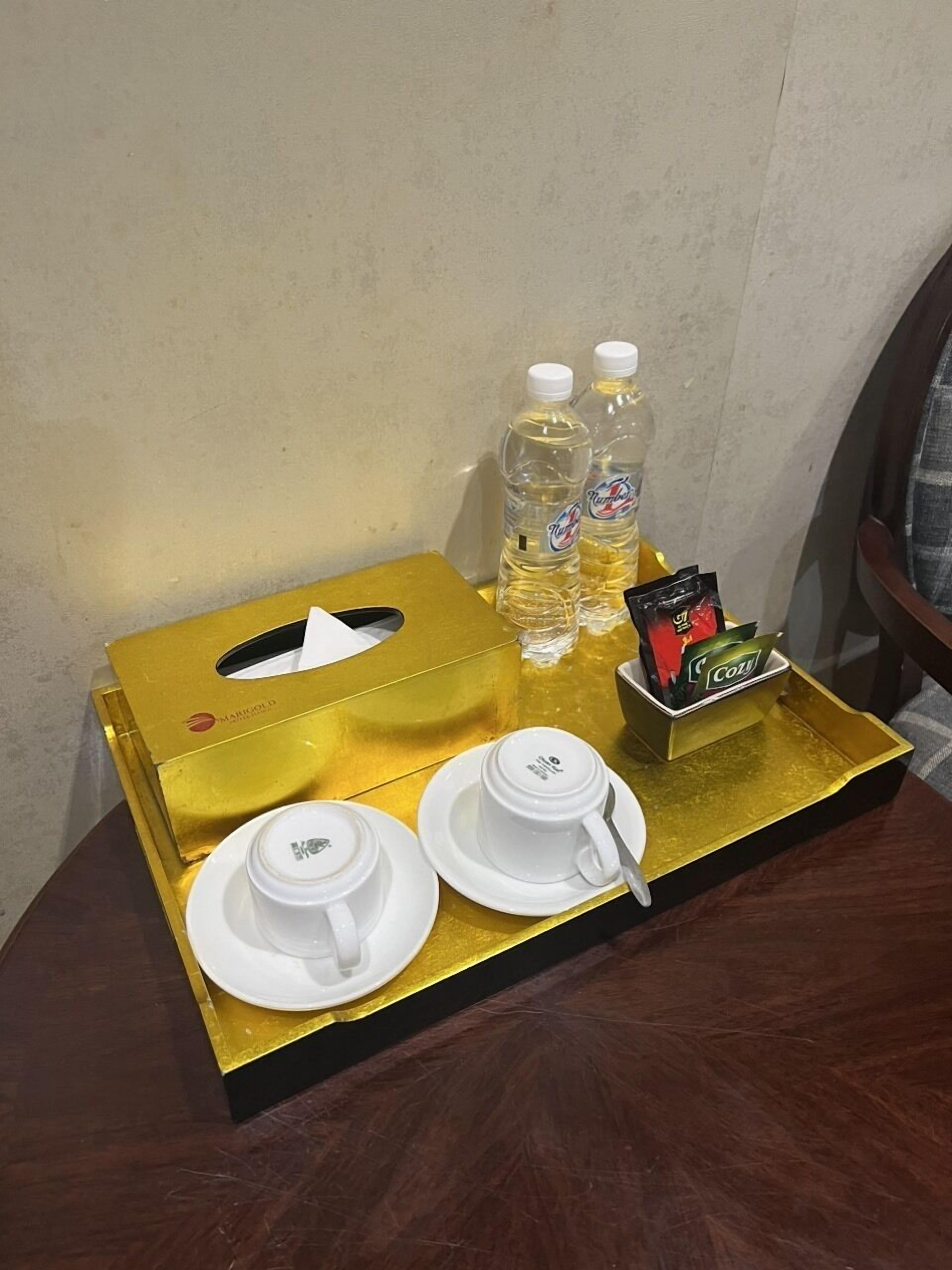 A tray with a tissue box, two cups, a spoon, two bottles of water, and a box of coffee on a wooden table.