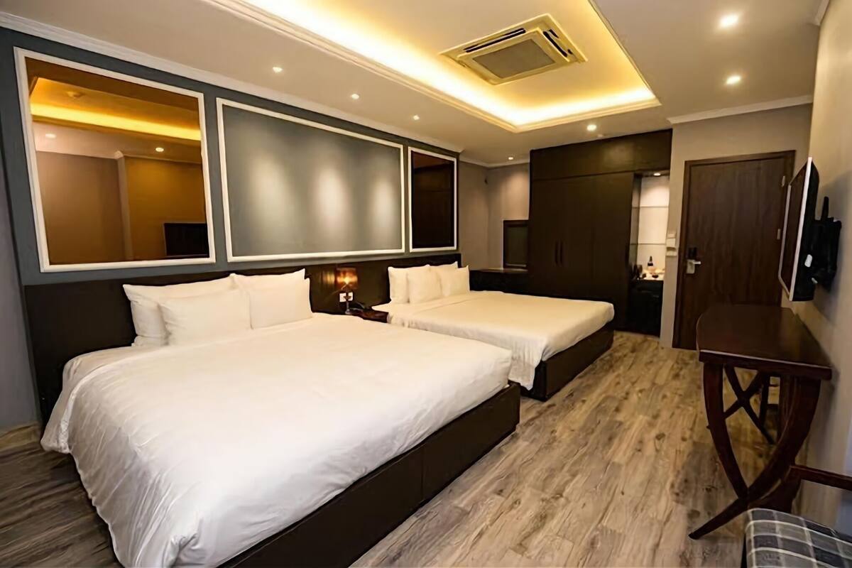 Ein Hotelzimmer mit zwei Betten, Holzboden, einem großen Spiegel und einem Fernseher.
