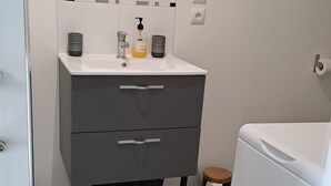 A bathroom with a white sink, a mirror, a towel dispenser, and a black trash bin.