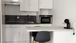 A modern kitchen with white cabinetry, a stainless steel range hood, a microwave, and a coffee machine.