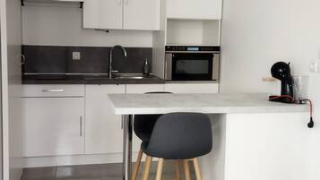 Une cuisine moderne avec des meubles blancs, une hotte en acier inoxydable, un four à micro-ondes et une machine à café.