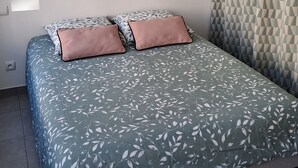 A bedroom with a bed, a hanging light fixture, a wall-mounted shelf, and a patterned curtain.