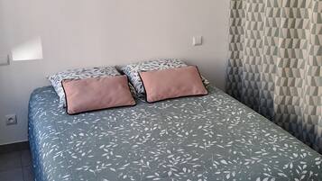 Une chambre à coucher avec un lit, un luminaire suspendu, une étagère fixée au mur et un rideau à motifs.