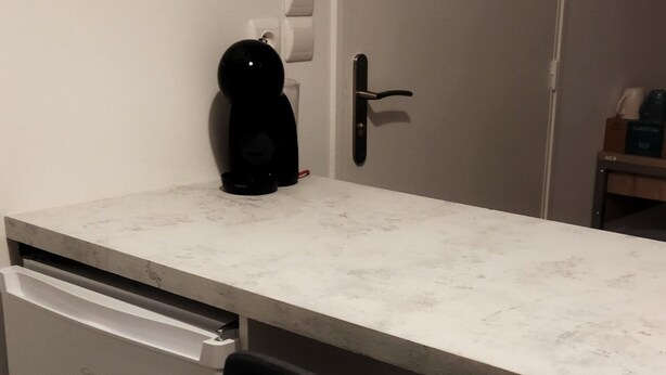 A compact kitchen with a white countertop, a black chair, and a white refrigerator.